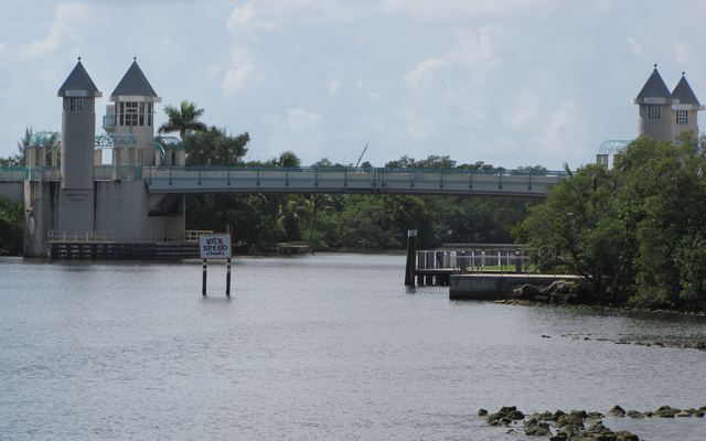 The Ocean Avenue drawbridge over the Intracoastal Waterway in Boynton Beach, with pointed-roof control towers at each end, mangroves along the shore and an Idle Speed sign standing in the water