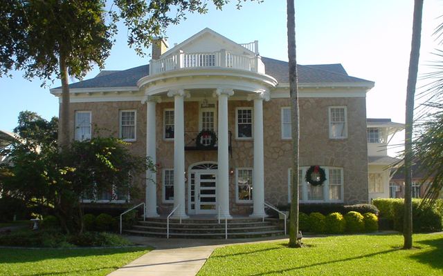 The Porcher House in Cocoa, a two-story coquina stone mansion with a curved portico of white columns, holiday wreaths on the windows and a palm-lined lawn