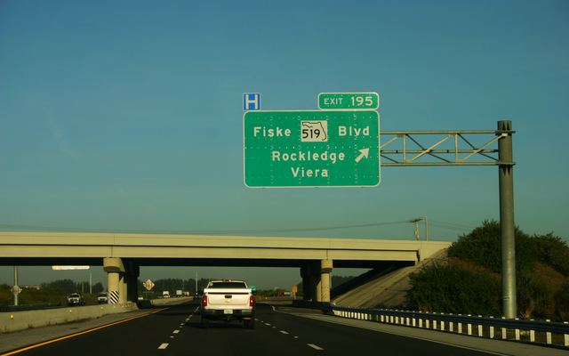 Green overhead sign on Interstate 95 for Exit 195, Fiske Boulevard, State Road 519, pointing to Rockledge and Viera, with a blue hospital sign beside it, an overpass ahead and a white pickup truck in the lane below