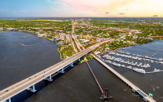 Aerial view of the Roosevelt Bridge crossing the St. Lucie River into Stuart, with the railroad drawbridge and a lower bridge beside it, a marina full of boats and the downtown streets beyond
