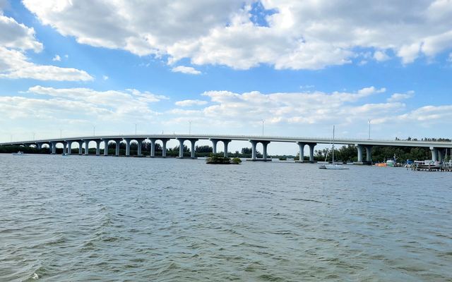 The Merrill P. Barber Bridge stretching across the Indian River Lagoon in Vero Beach under white clouds, with a sailboat and boat docks on the right