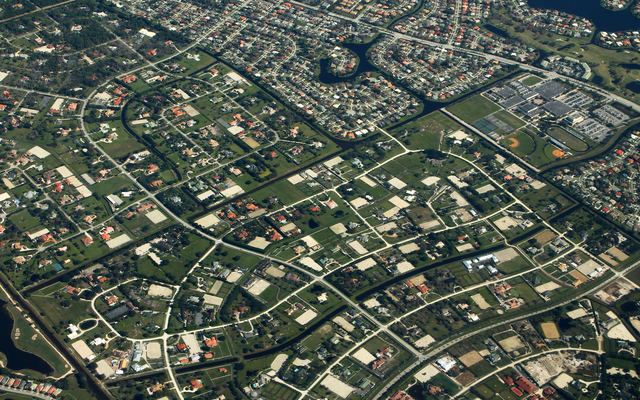 Aerial view of Wellington, Florida: large equestrian lots with sand riding arenas, divided by canals and tree-lined roads, with curving subdivisions, a lake and ball fields beyond